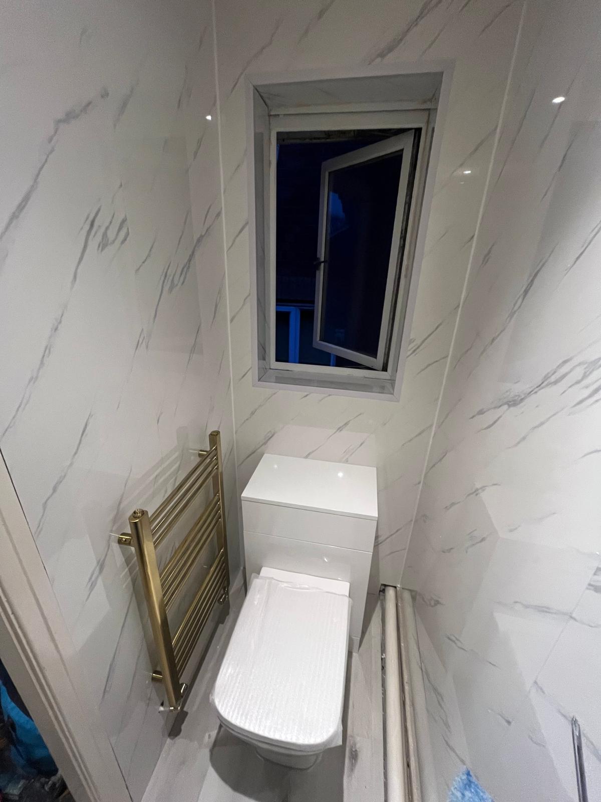 Completed downstairs WC in Lytham St Anne's with marble-effect wall panels, concealed cistern toilet and brushed gold heated towel rail