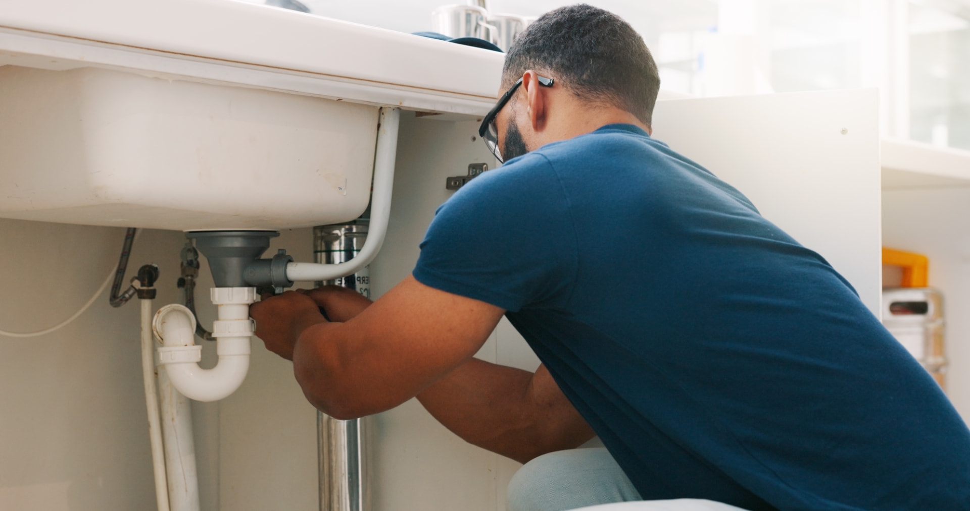 Plumber repairing a sink waste trap and pipework under a kitchen sink