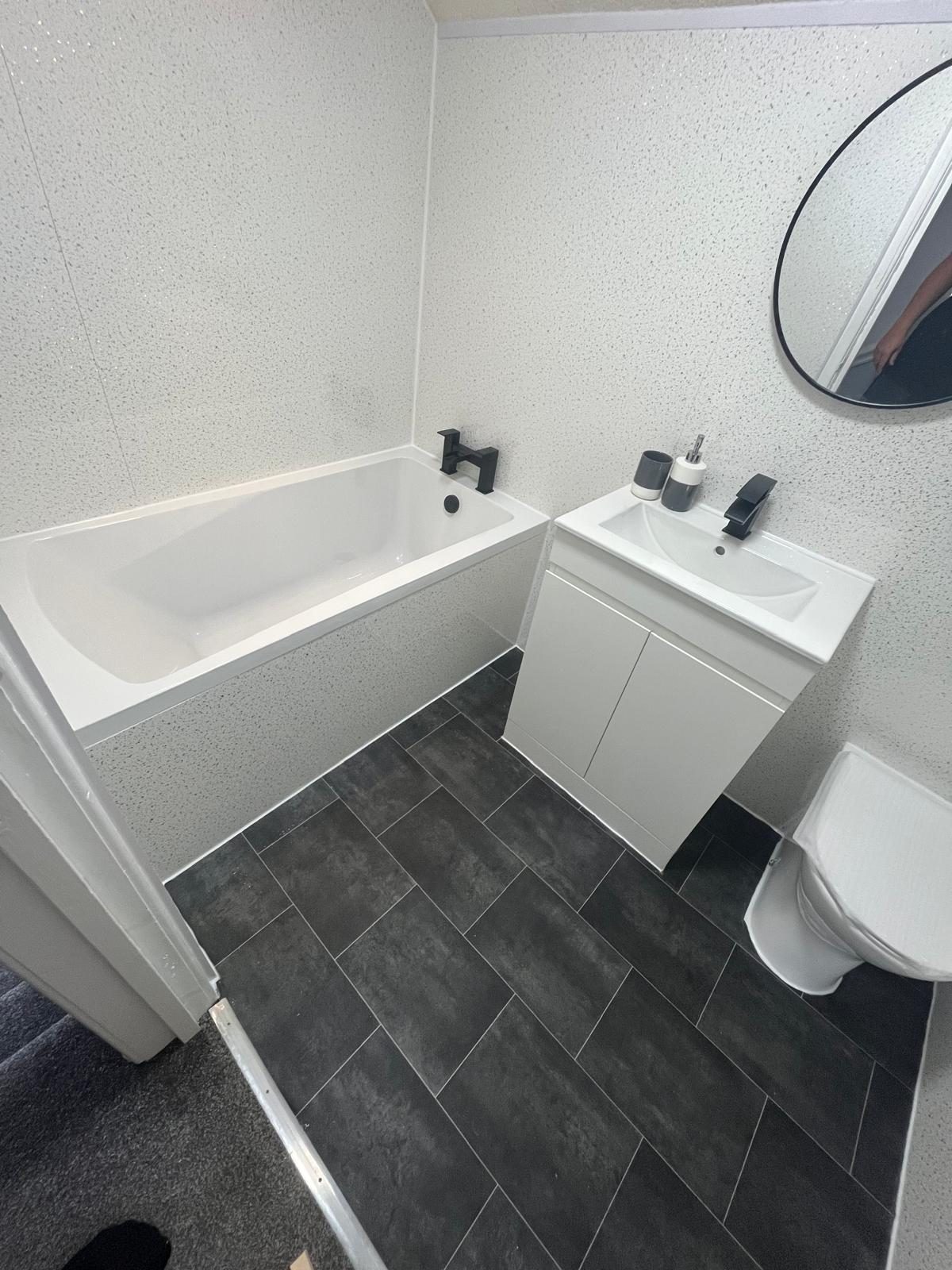 Modern bathroom renovation with white bath, vanity basin, black taps and dark floor tiles