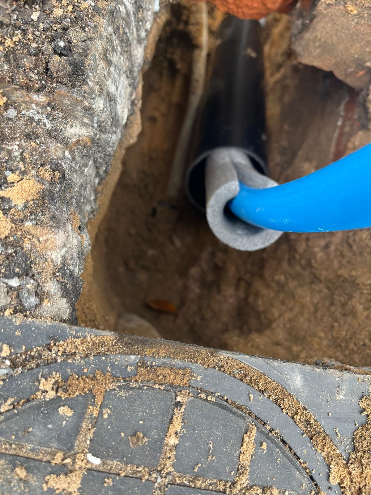 Leak detection work exposing a blue MDPE water pipe connection beside brickwork