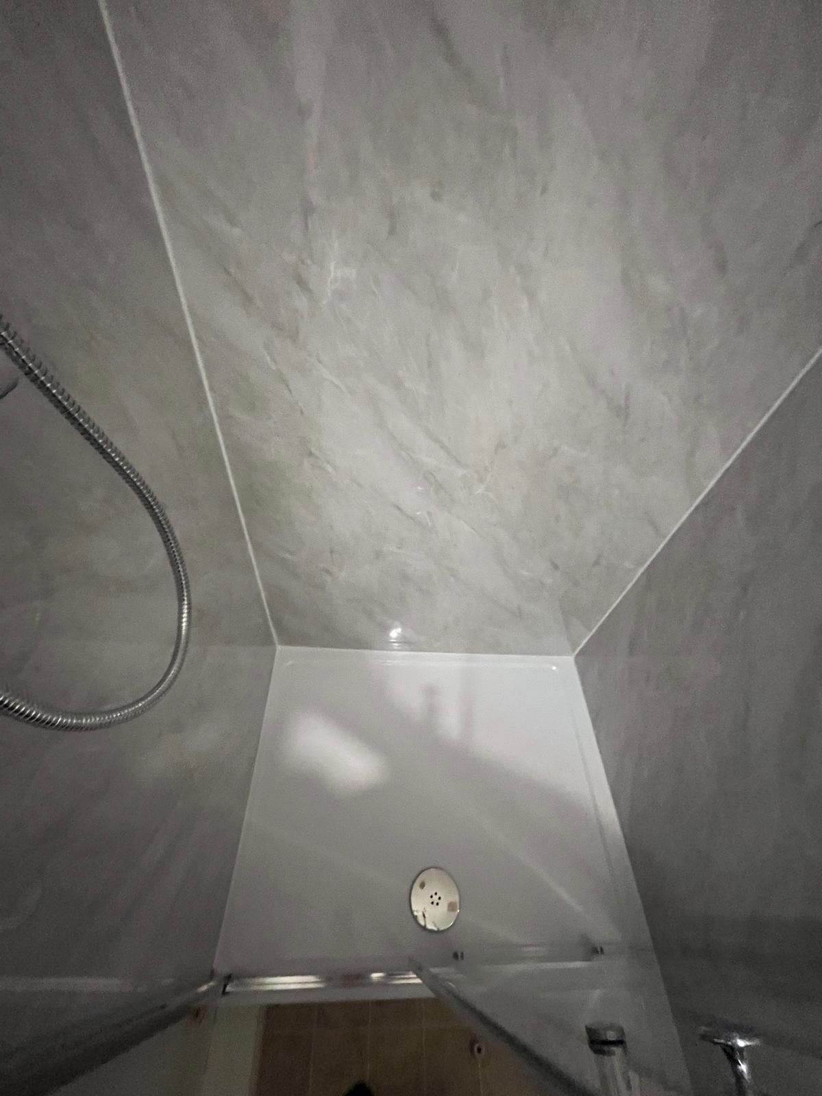 Newly fitted shower tray and marble-effect wall panels in a compact shower cubicle