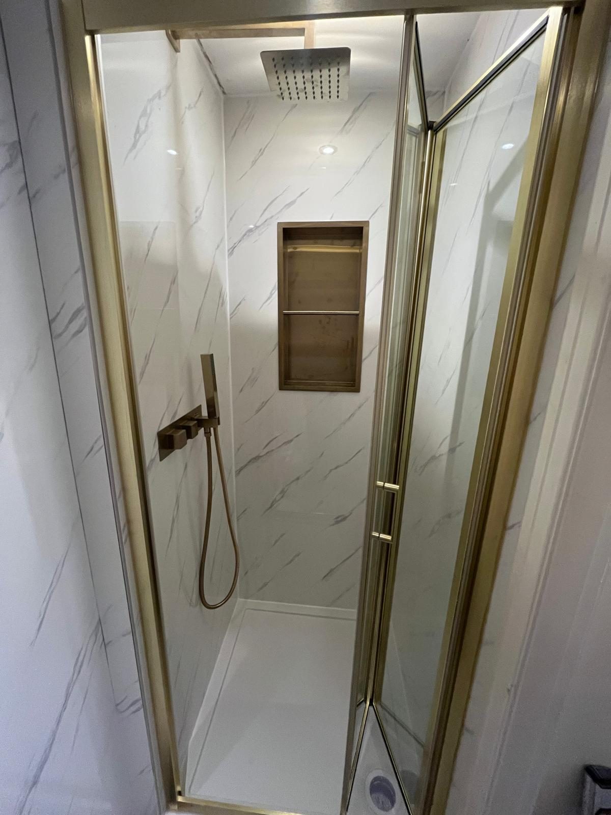 Shower enclosure installation with gold framed bi-fold door and recessed shelf niche