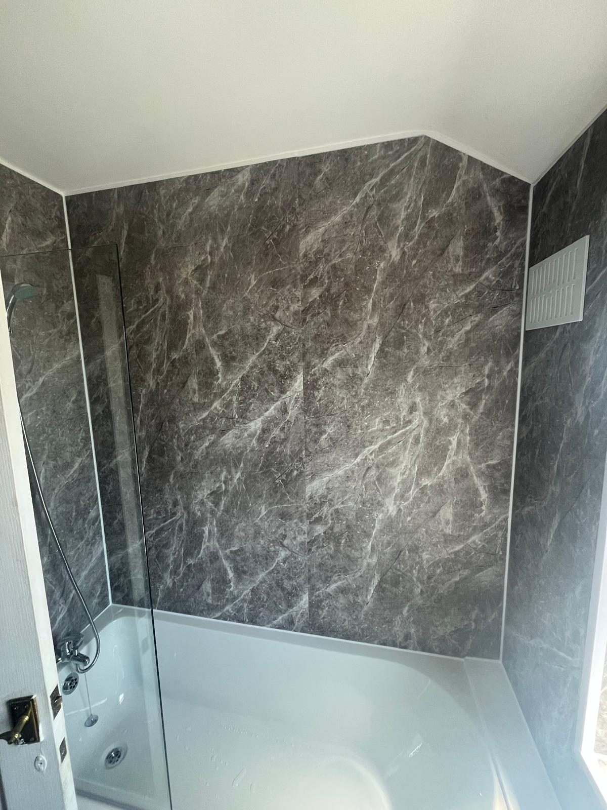 Bath fitted with dark marble-effect surround and glass shower screen by Pro Plumbing Solutions