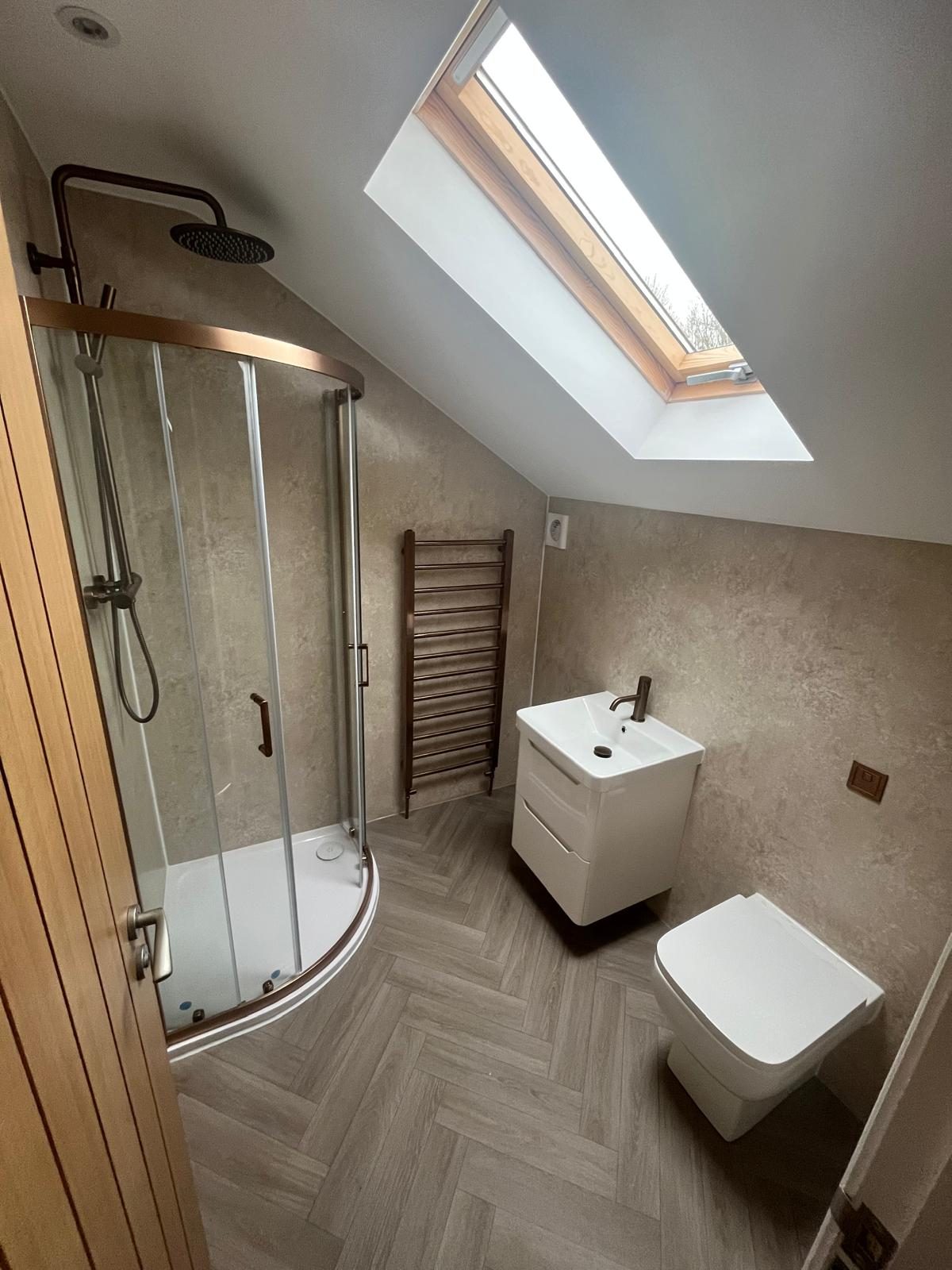 Finished loft bathroom with curved shower, wall-hung basin and herringbone flooring