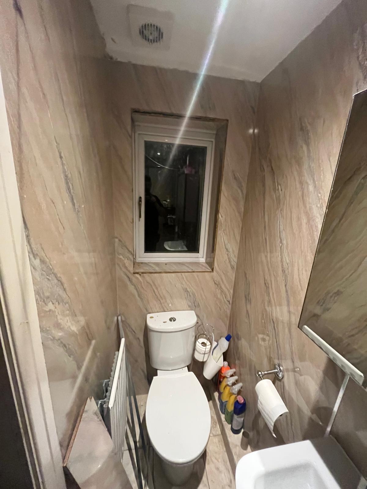 The same downstairs WC before renovation, with dated beige marble-effect panelling, close-coupled toilet and old radiator