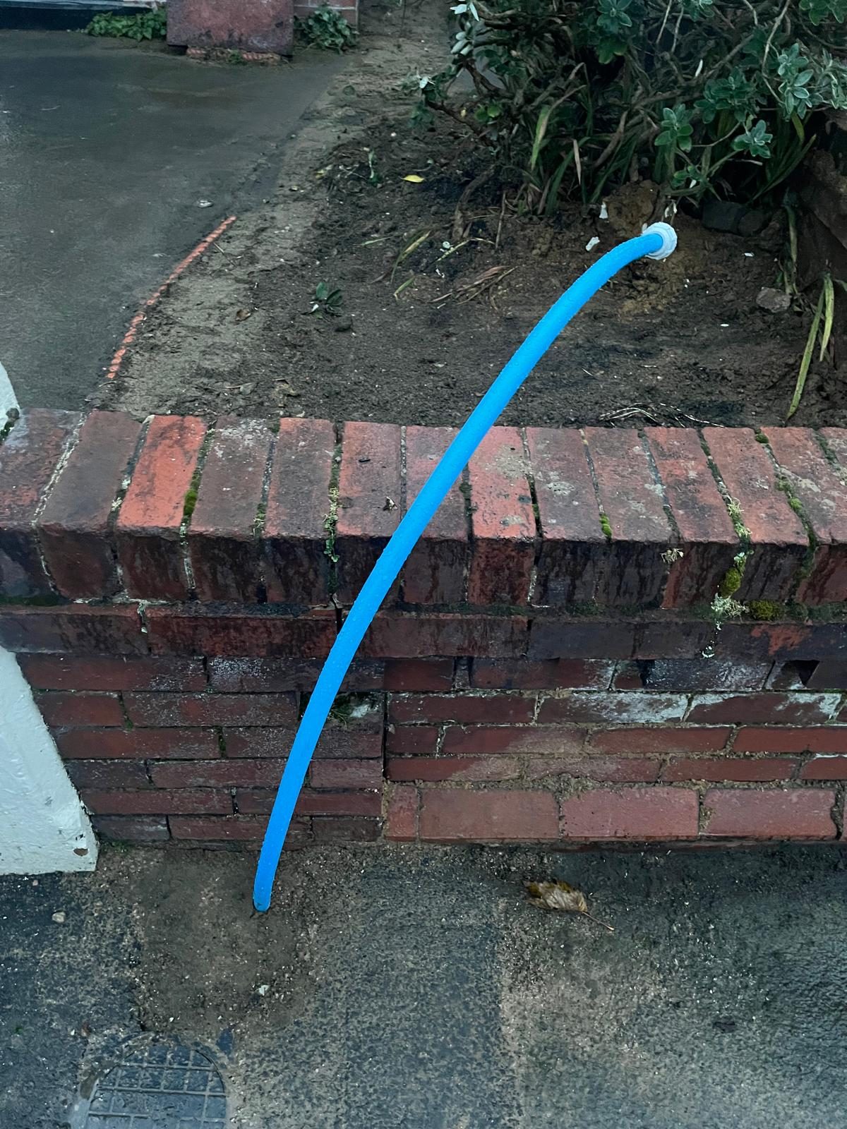 New blue water supply pipe routed over a garden wall following leak detection