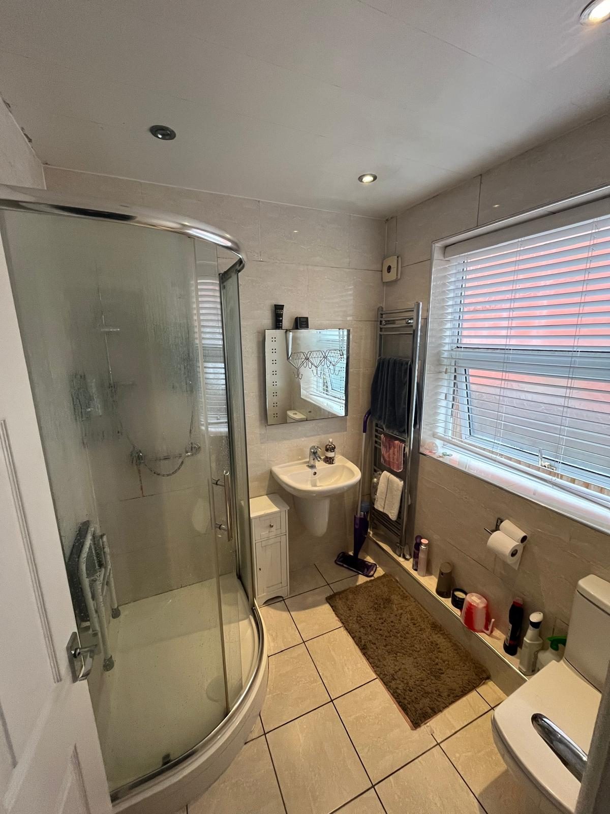 Bathroom with curved shower enclosure, pedestal sink and towel radiator before upgrade work