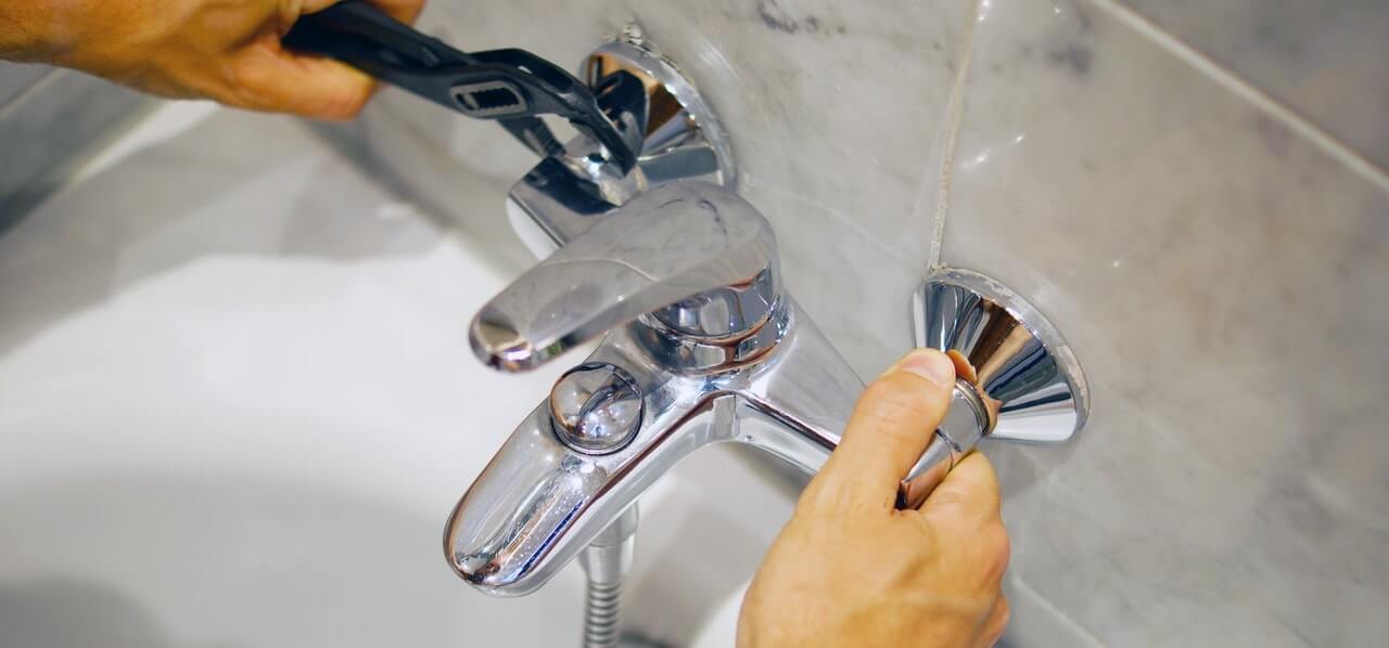 Plumber tightening a chrome bath tap during a tap and stopcock repair